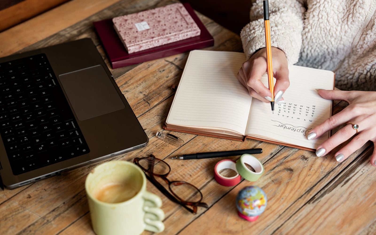A woman planning in a notebook beside a laptop and coffee