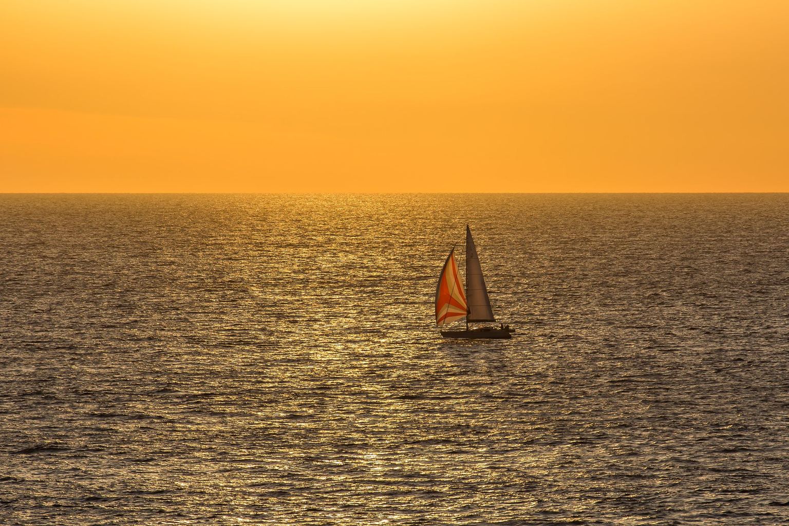 A sailboat under full sail off the Carolina coast at golden hour