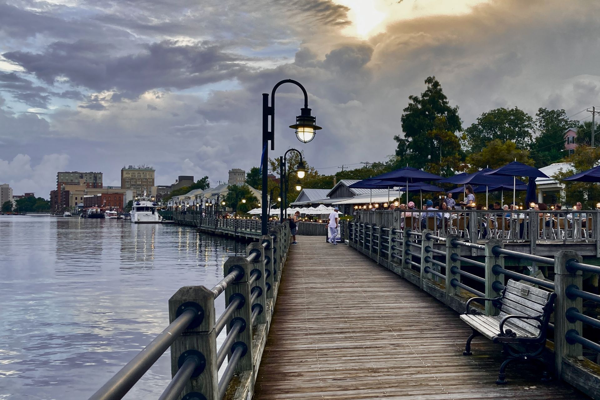 Wilmington's Riverwalk boardwalk at dusk, with waterfront lamps lit and downtown in the distance