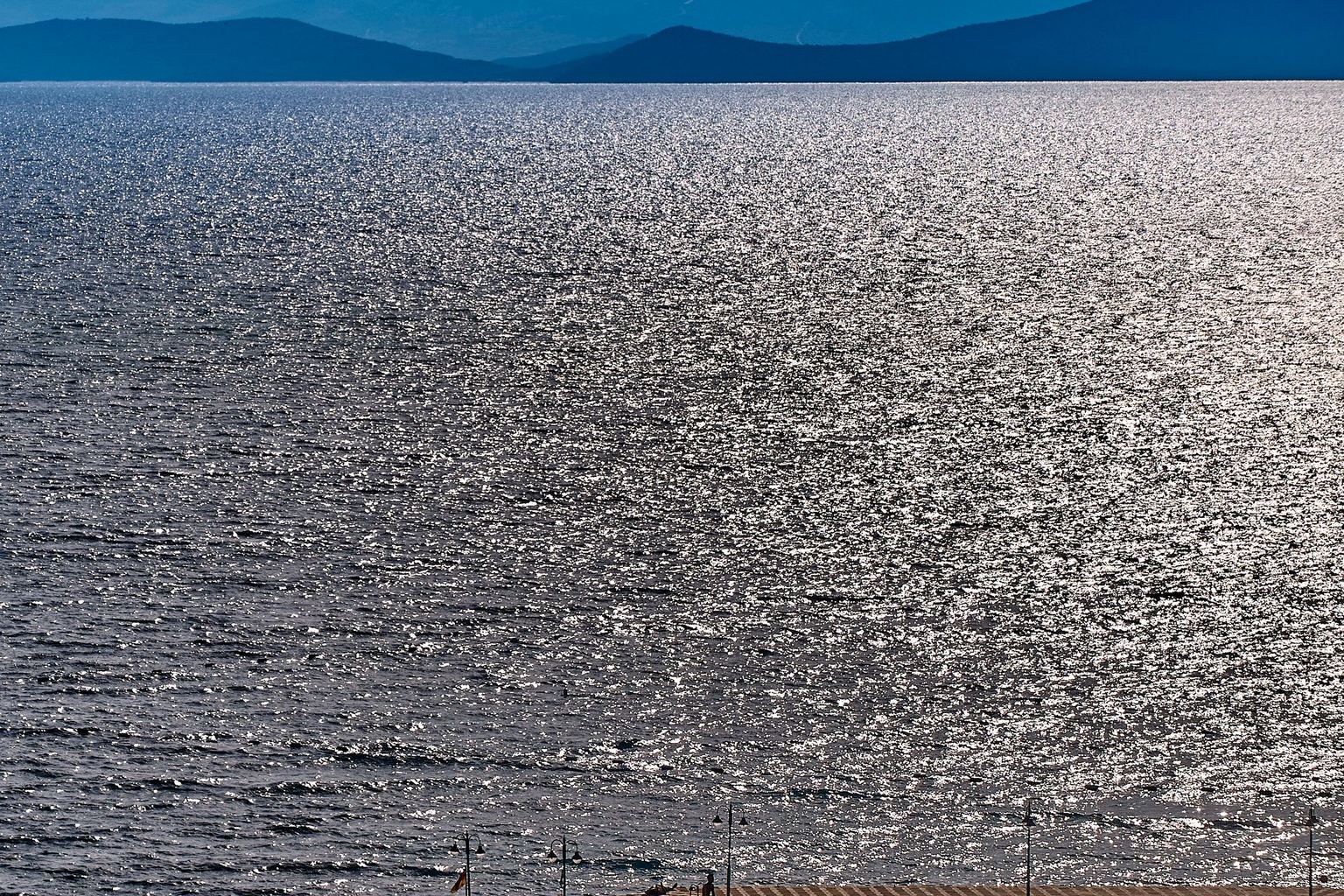 A wooden pier reaching into calm ocean water on a bright afternoon